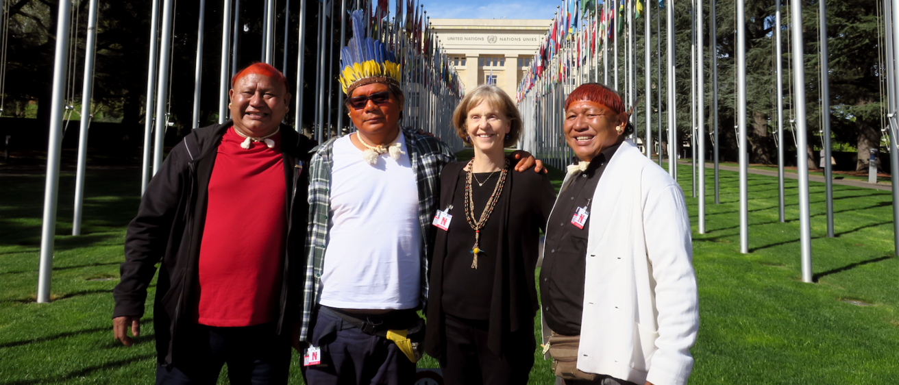 Four members of an anthropological outreach team standing together in front of a row of international flags.